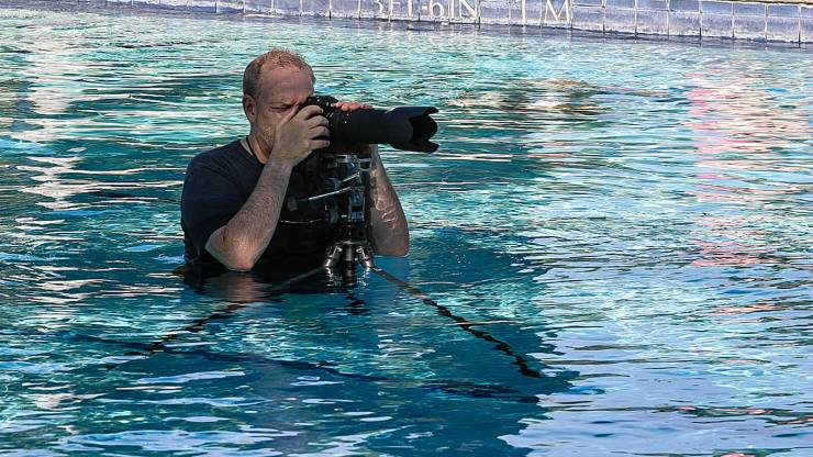 Kevin Ames avec un appareil photo reflex numérique sur un trépied dans une piscine photographiant un éditorial de maillot de bain